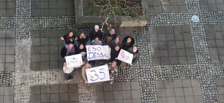 Gruppe von Schüler*innen steht auf einem gepflasterten Innenhof und hält selbst gestaltete Plakate mit „ESO Dessau“ und „35“ in die Kamera.