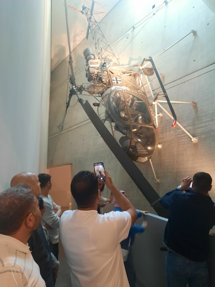 Spannende Exkursion ins Militärhistorische Museum Ein Blick von unten auf eine Gruppe von Menschen, die einen an einer Wand hängenden Militärhubschrauber in einem Museum betrachten. Einige Personen machen Fotos des Exponats.