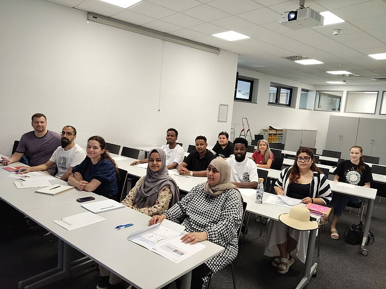 Gruppe IK-359 zu Besuch im BIZ Teilnehmende des Integrationskurses sitzen gemeinsam an Tischen in einem Seminarraum und arbeiten mit Informationsmaterialien.