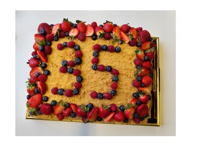 Rechteckiger Kuchen mit Beeren dekoriert, auf dessen Oberfläche die Zeichen „B1“ aus Himbeeren und Blaubeeren gelegt sind.