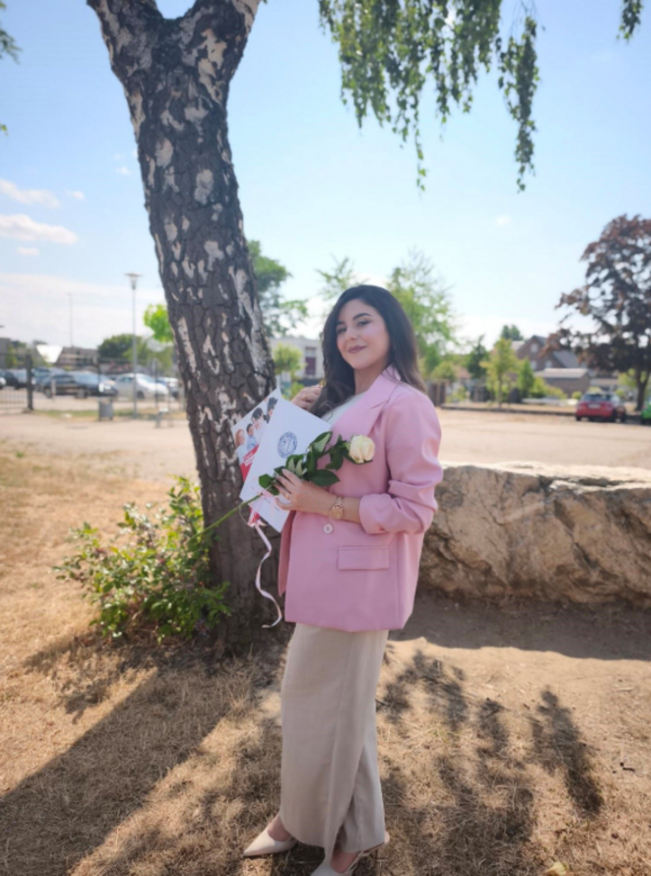 Eine junge Frau in einem rosa Jaquette posiert vor einem Baum und lächelt