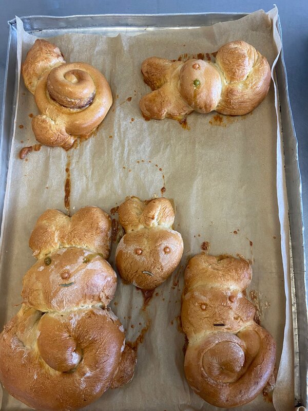 Auf einem Backblech liegen fünf gebackene Osterhasen aus Hefeteig.