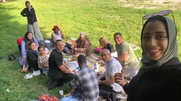 Teilnehmende sitzen auf Decken zu einem kleinen Picknick auf einer Wiese beisammen.