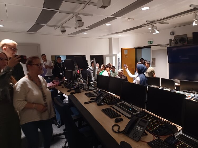 Die Teilnehmenden der Euro-Schulen Mainz sehen sich im Aufnahmeraum des Fernsehstudios um, in dem viele Bildschirme und Computer sowie Telefone stehen.