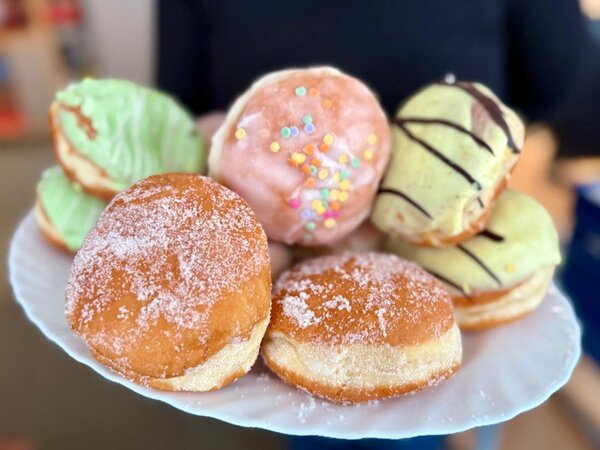 Teller mit verschiedenen Berlinern in bunten Glasuren und Zuckerguss, serviert zum Fasching am 11.11.2025 um 11:11 Uhr während einer Pause an den Euro-Schulen und den Euro Akademien Dresden, Meißen und Riesa. Die Süßspeisen schaffen, zusätzlich zur närrischen Jahreszeit, eine besondere Wohlfühlatmosphäre im Schulalltag.