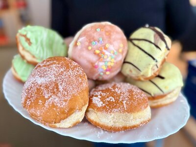 Teller mit verschiedenen Berlinern in bunten Glasuren und Zuckerguss, serviert zum Fasching am 11.11.2025 um 11:11 Uhr während einer Pause an den Euro-Schulen und den Euro Akademien Dresden, Meißen und Riesa. Die Süßspeisen schaffen, zusätzlich zur närrischen Jahreszeit, eine besondere Wohlfühlatmosphäre im Schulalltag.