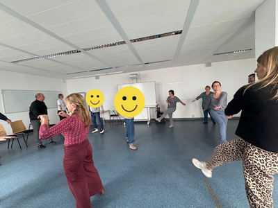 Rück’n’Roll – Bring Bewegung in dein Leben! In einem großen Raum stehen die Teilnehmenden des Gesundheitstages im Kreis und heben das gestreckte Bein quer nach oben.