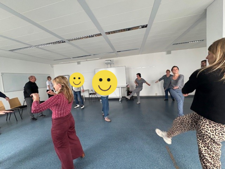 Rück’n’Roll – Bring Bewegung in dein Leben! In einem großen Raum stehen die Teilnehmenden des Gesundheitstages im Kreis und heben das gestreckte Bein quer nach oben.