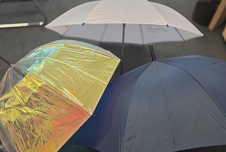 Zwischen Cocktail- und Regenschirm Drei verschiedenfarbige Regenschirme, die in einem Büro aufgestellt sind, geben Zeugnis von einem verregneten Sommer.