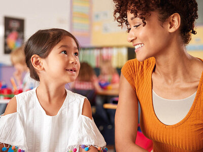 Eine Kind und eine Frau mit orangenem Oberteil sitzen nebeneinander und lächeln.