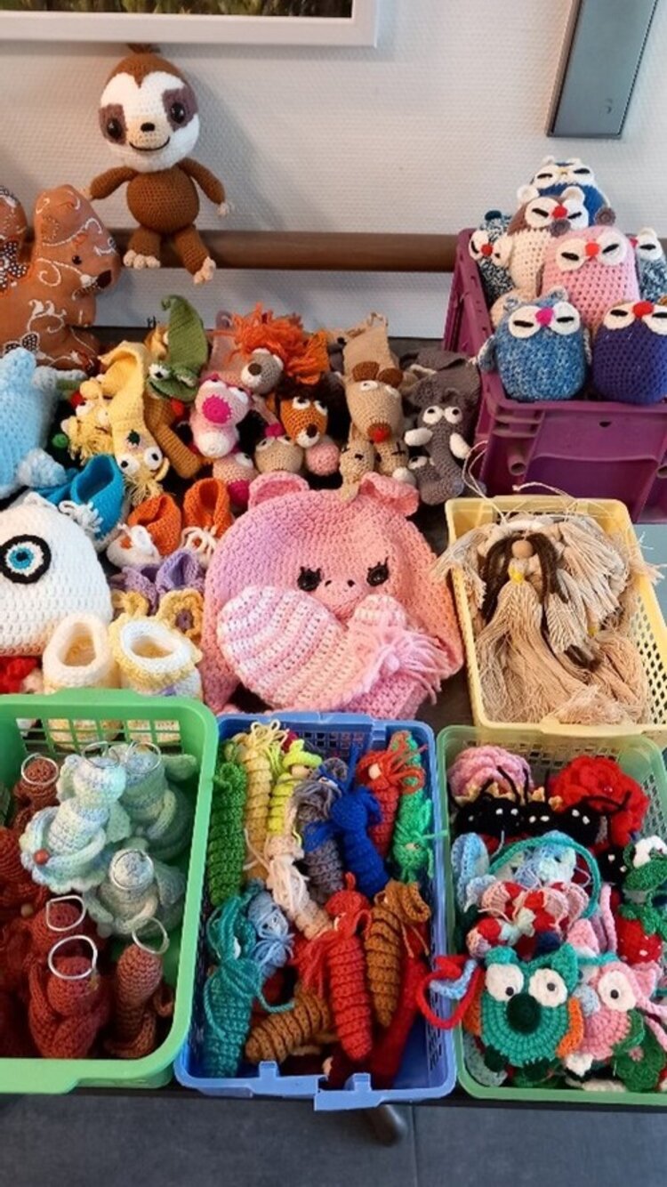 Viele bunte, handgemachte Tiere aus Wolle, wie Eulen, Mäuse und Puppen liegen in bunten Körben auf einem Tisch.