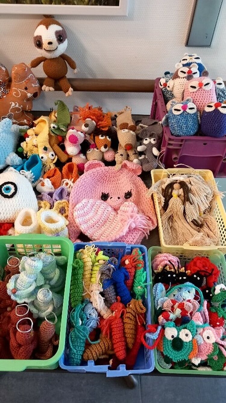 Viele bunte, handgemachte Tiere aus Wolle, wie Eulen, Mäuse und Puppen liegen in bunten Körben auf einem Tisch.