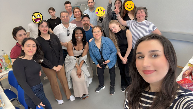 Gruppen-Selfie eines B2-Kurses in einem Klassenraum; mehrere Teilnehmende stehen eng zusammen und lächeln in die Kamera, einige Gesichter sind mit Smileys verdeckt.