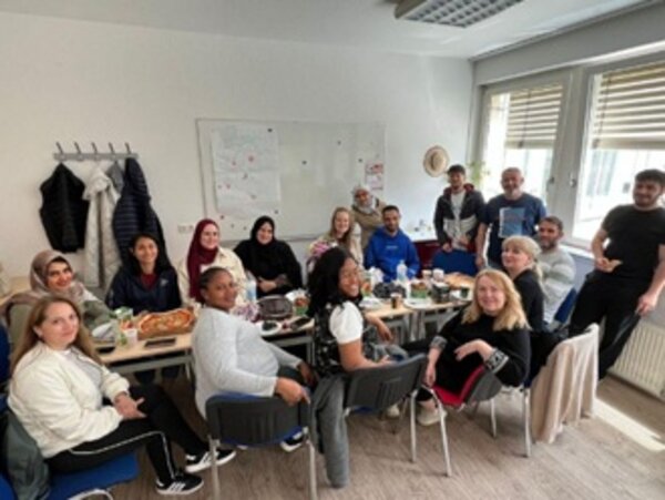 Mitarbeitende der Euro-Schulen Potsdam sitzen gemeinsam an einem gedeckten Tisch und verabschieden ihre Kollegin in den Mutterschutz.