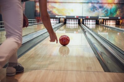 Auf einer Bowlingbahn wird eine Arm mit einer Bowlingkugel Richtung der Pins.