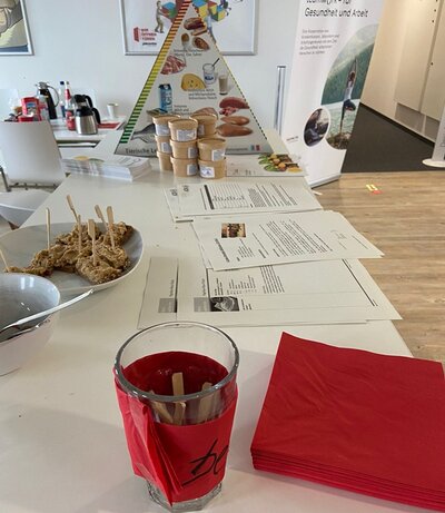 Langer Tisch, mit vielem Informationsbroschüren, einem Aufsteller, der die Nahrungspyramide zeigt und gesunden Snackriegeln.