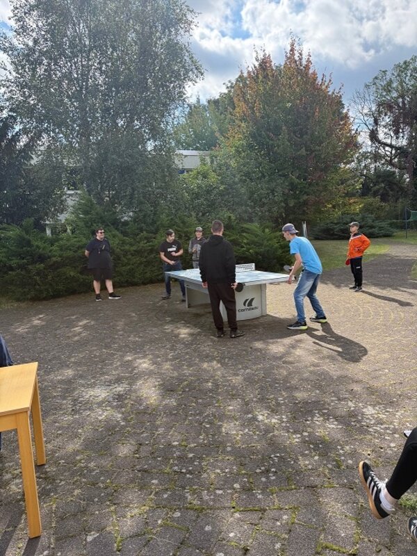 Mehrere Azubis spielen auf einem Außengelände Tischtennis.