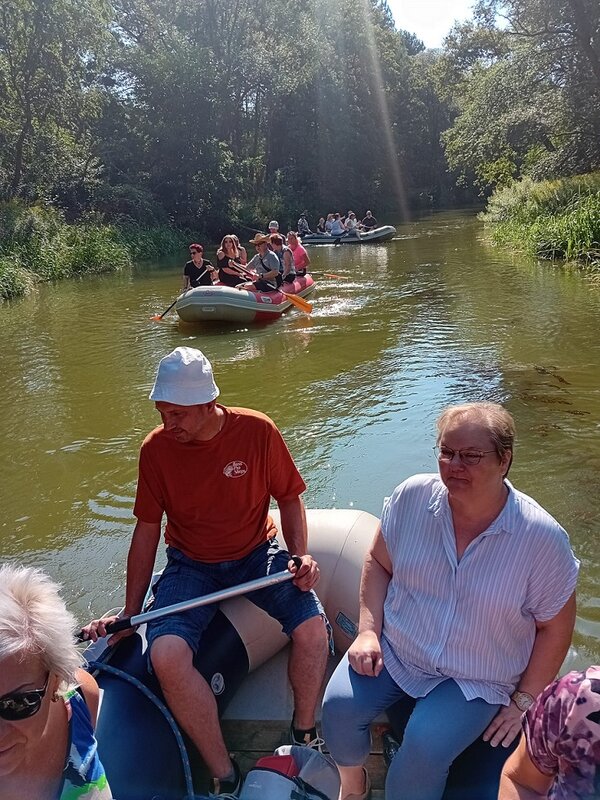Drei Boote fahren auf einem kleinen Fluss. Das Bild ist vom ersten Schlauchboot aus aufgenommen, darin sieht man drei Personen sitzen. Das zweite Boot fährt in Fließrichtung des Stroms, das dritte hingegen steht quer zum Fluss.