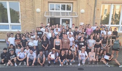 Ein große Gruppe von Schülerinnen, Schülern und Lehrkräften in Sportkleidung hat sich zu einem Gruppenbild vor dem Eingang des Schulgebäudes versammelt.