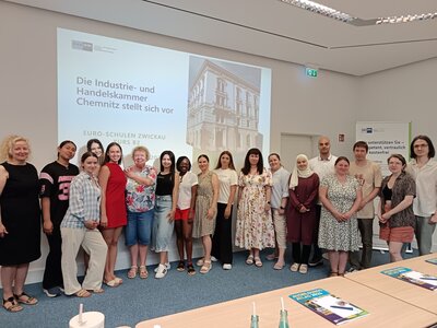 Teilnehmende des B2-Kurses der Euro-Schulen Zwickau stehen gemeinsam nach einer Präsentation der Industrie- und Handelskammer Chemnitz vor einer Leinwand.