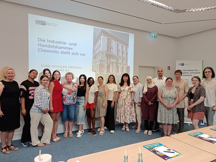 Teilnehmende des B2-Kurses der Euro-Schulen Zwickau stehen gemeinsam nach einer Präsentation der Industrie- und Handelskammer Chemnitz vor einer Leinwand.