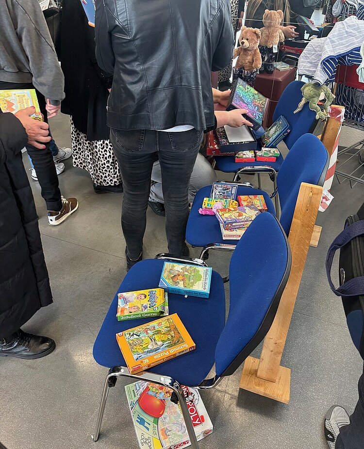 Unser Nachhaltigkeitsbasar ist immer ein Highlight Auf blauen Stühlen sind verschiedene Spiele und Puzzle ausgelegt. Der Andrang bei den Betrachtenden ist groß.