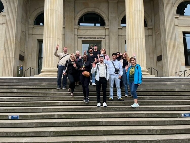 Politik hautnah erleben Eine Gruppe junger Menschen steht auf den Stufen vor dem niedersächsischen Landtag und winkt in die Kamera.