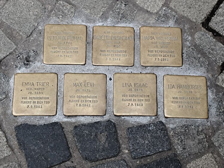 Sieben Stolpersteine im Kopfsteinpflaster mit eingravierten Namen und Daten zur Erinnerung an verfolgte jüdische Menschen; die Messingplatten sind in zwei Reihen angeordnet.