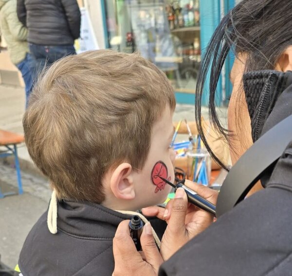 Eine Frau schminkt einem Jungen ein rotes Spiderman-Gesicht auf die Wange.