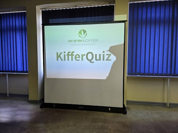 Auf einer Leinwand ist das „KifferQuiz“ des Projekts „Der grüne Koffer“ zu sehen.