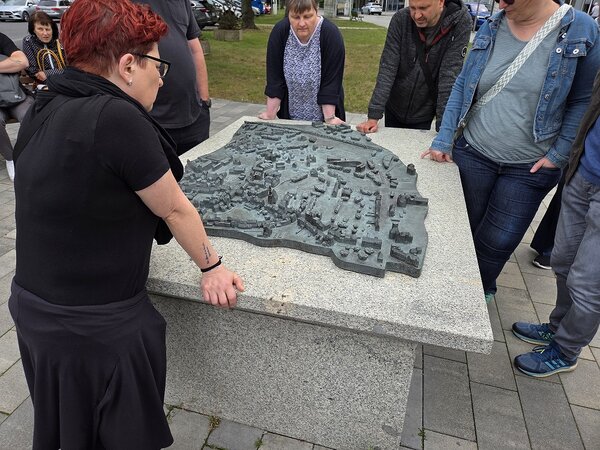 Eine Menschengruppe steht um einen Steinsockel, auf dem ein Miniaturmodell der Stadt Hoyerswerda steht.