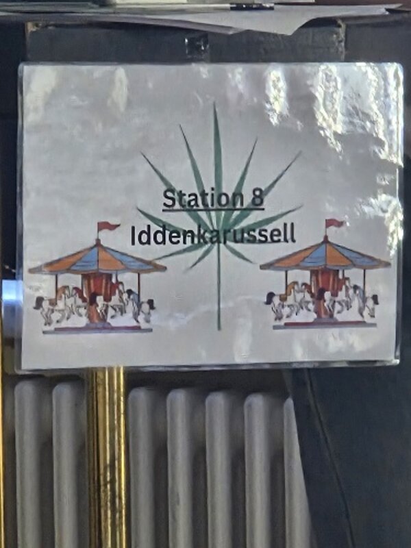 Schild mit der Aufschrift „Station 8 – Ideenkarussell“, verziert mit zwei Karussell-Abbildungen.