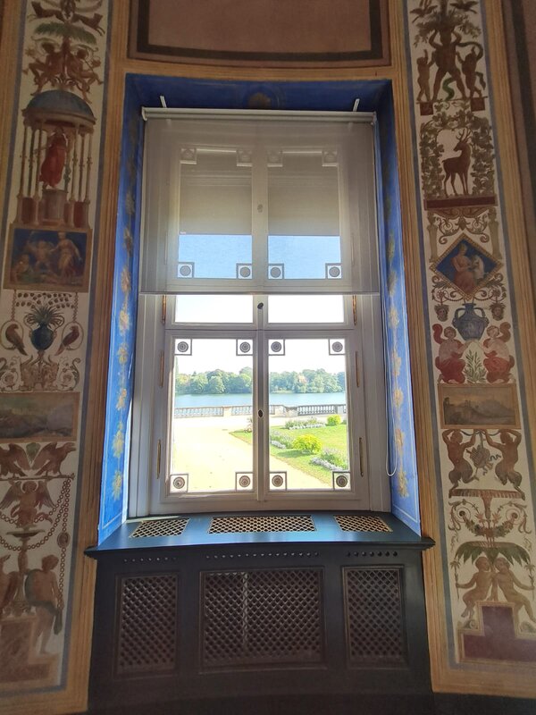 Aufnahme von einem Fenster in einem Schloss von innen nach außen. Die Seitenwände rechts und links vom Fenster sind mit Malereien verziert.