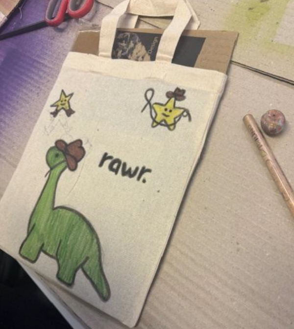 Selbst gestalteter Stoffbeutel mit einem grünen Dinosaurier und zwei kleinen Sternfiguren. Daneben steht der handgeschriebene Schriftzug „rawr“.