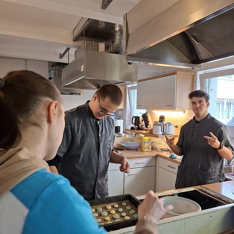 Drei Auszubildende stehen in einer Großküche und backen Plätzchen.