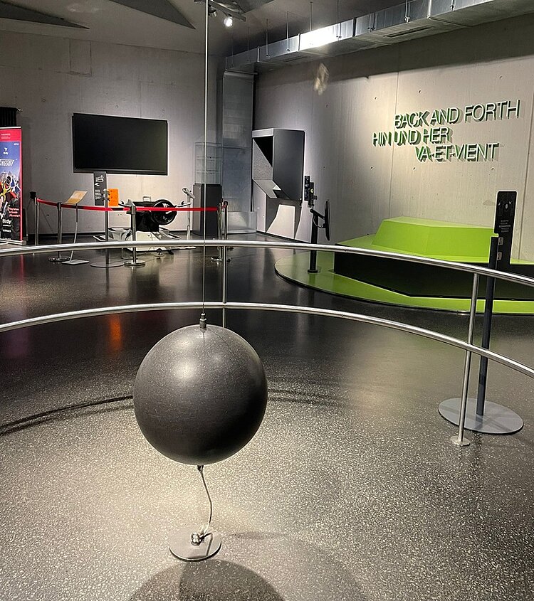 Erfolgreiches Bildungs-Speed-Dating Blick in einen Saal der Phänomenta, in der eine Installation einer Kugel hängt, an der Wand die Schriftzüge "Back And Forth", "Hin und Her", "Va-Et-Vientt".