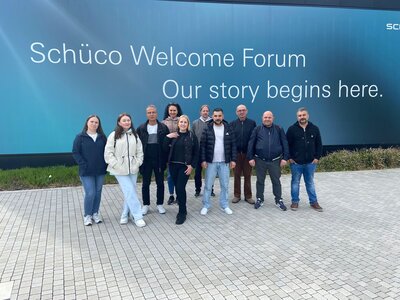 Gruppenbild draußen vor einer blauen Wand, auf der steht "Schüco Welcome Forum - Our story begings here."