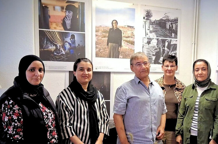 Fünf Personen stehen gemeinsam vor einer Fotoausstellung mit großformatigen Porträts und dokumentarischen Aufnahmen.