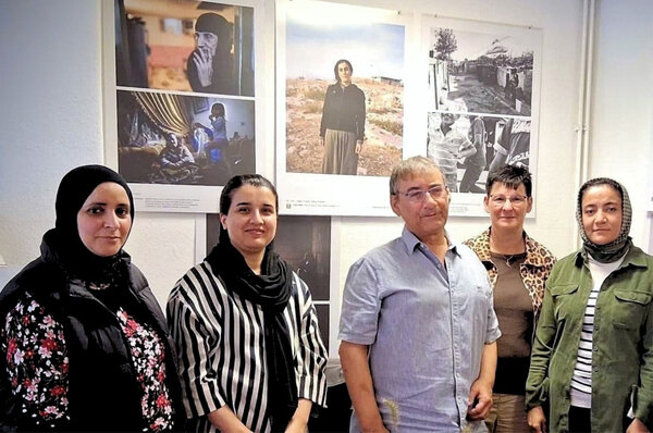 Fünf Personen stehen gemeinsam vor einer Fotoausstellung mit großformatigen Porträts und dokumentarischen Aufnahmen.