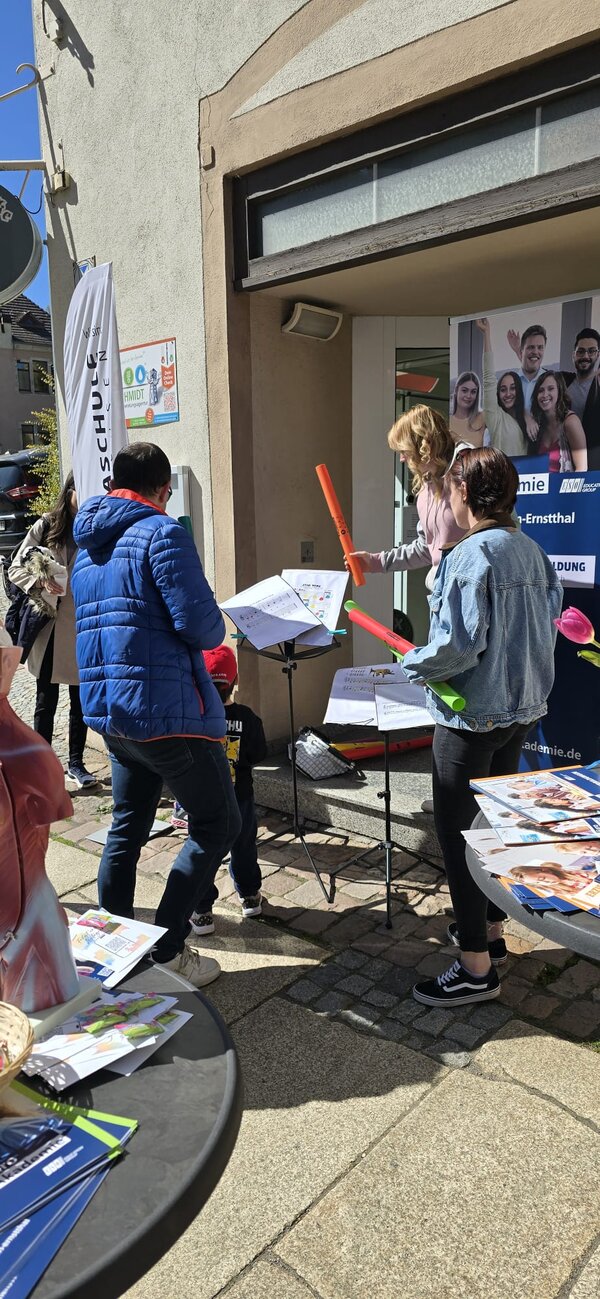 An einem Infostand der Euro Akademie Hohenstein-Ernstthal stehen drei Menschen mit Boomwhackern, bunten Stäben zum Musikmachen, vor Notenständern.