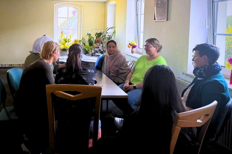 Mehrere Frauen sitzen in einem hellen Raum gemeinsam an einem Tisch und tauschen sich in einer Gesprächsrunde aus.