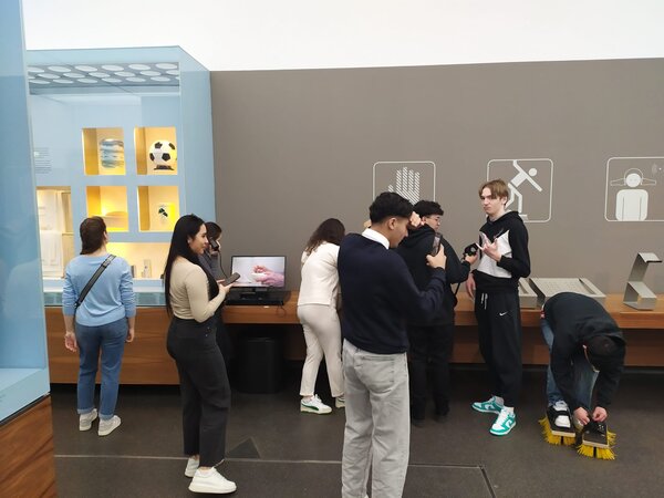 Eine Gruppe von Menschen erkundet eine Ausstellung mit interaktiven Elementen. Einige nehmen an Experimenten teil, während andere sich umschauen oder Fotos machen.