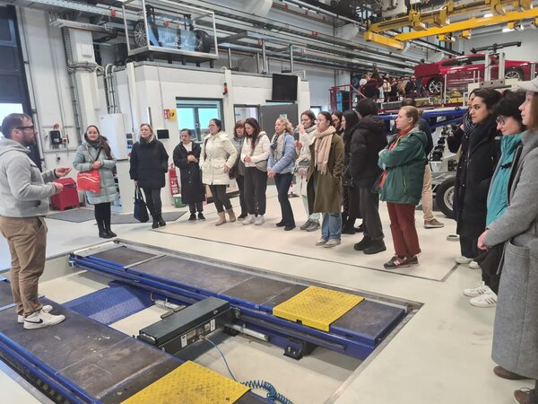 Die Schülerinnen und Schüler stehen um eine Hebebühne herum und schauen bei einer Montage zu.