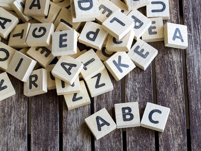 Mehrere Holzwürfel mit verschiedenen Buchstaben des Alphabets liegen verstreut auf einer Holzoberfläche. Im Vordergrund sind die Buchstaben 'A', 'B' und 'C' sichtbar.