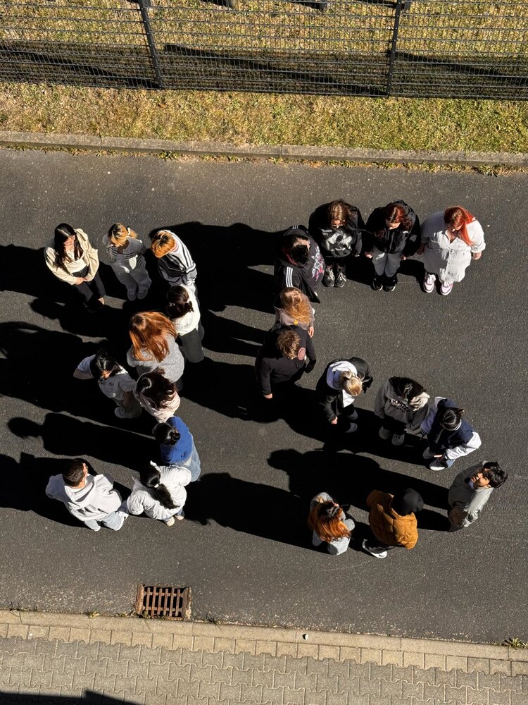 Sicht von oben auf eine Menschengruppe, die auf einer sonnenbeschienenen Straße die Zahl 35 bildet.