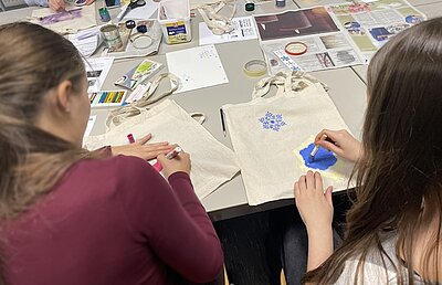 Berufsorientierung an der Euro Akademie Leipzig Zwei Schülerinnen sitzen an einem Tisch voller Bastelutensilien und bemalen Stofftaschen.