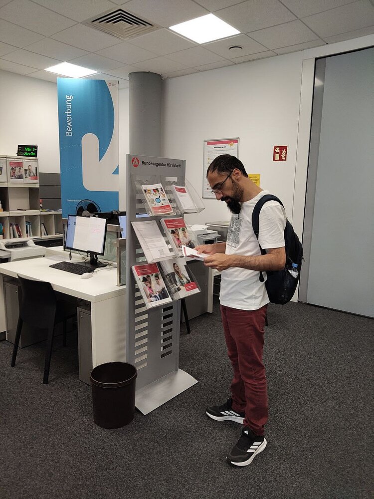 Gruppe IK-359 zu Besuch im BIZ Ein Teilnehmer des Integrationskurses liest konzentriert Informationsbroschüren am Regal des Berufsinformationszentrums.