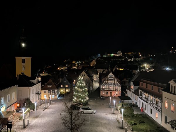 Blick über einen beleuchteten Altstadt-Marktplatz bei Nacht mit Weihnachtsbaum, Fachwerkhäusern und Kirche im Hintergrund.