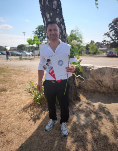Ein Mann in weißem Shirt posiert mit einer Urkunde vor der Kamera.