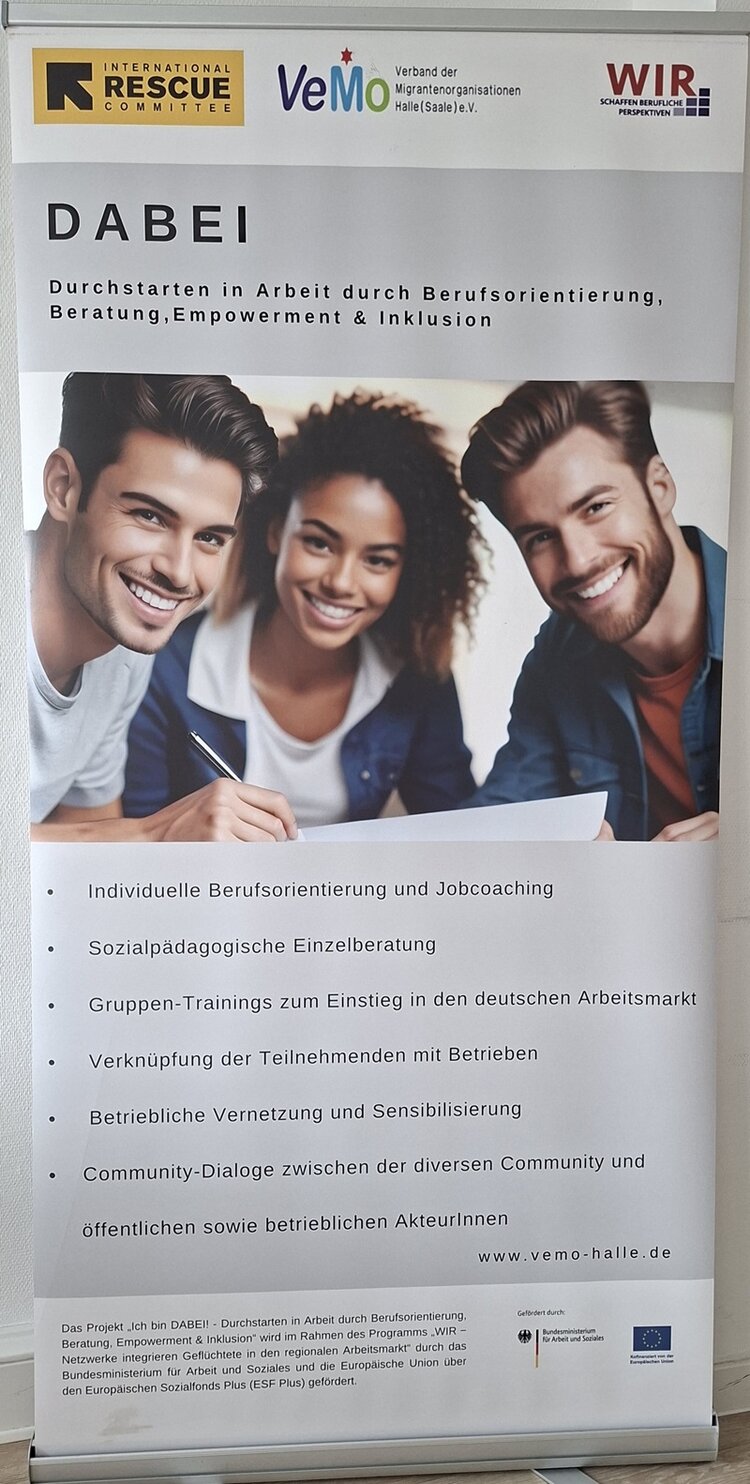 Ein Roll-up-Banner zeigt oben die Logos von drei Organisationen auf weißem Hintergrund. Darunter steht in großen Buchstaben das Wort 'DABEI', gefolgt von einem erklärenden Text zur beruflichen Orientierung und Inklusion. Im mittleren Bereich ist eine farbige Fotografie von drei Personen zu sehen, die an einem Tisch sitzen und gemeinsam auf Unterlagen blicken. Im unteren Bereich folgt eine Liste mit sechs Angeboten, darunter individuelle Berufsorientierung, sozialpädagogische Einzelberatung und Community-Dialoge. Am unteren Rand befinden sich weitere Logos und ein Hinweis auf die Förderung durch die Europäische Union.